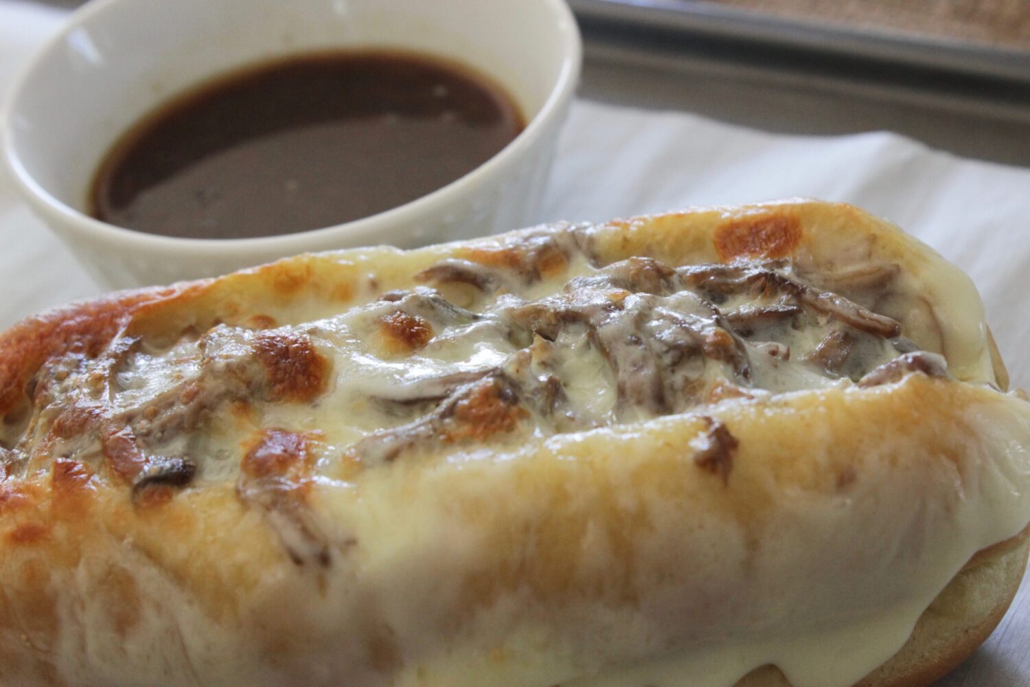 Crock pot French dip sandwich on a hoagie with a cup of au jus for dipping