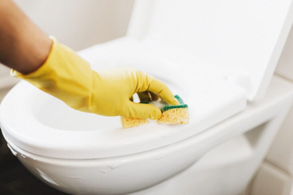Gloved hand scrubbing a white toilet with a sponge — cleaning the toilet bowl with borax
