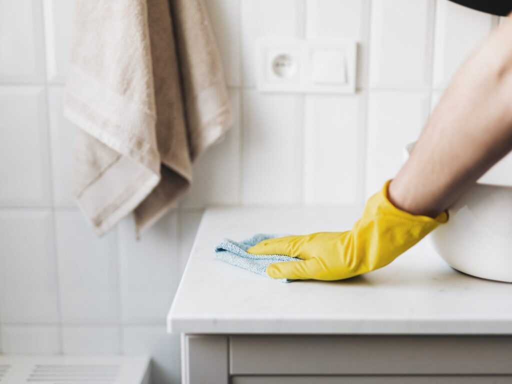 Gloved hand wiping a bathroom counter with a microfiber cloth — cleaning with hydrogen peroxide