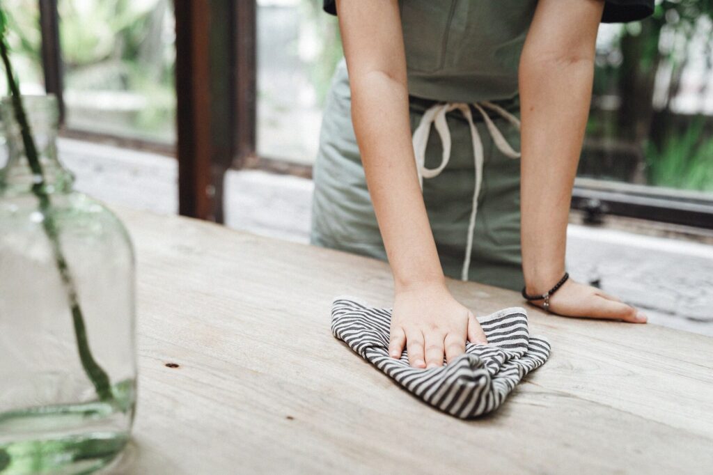 Hand wiping down a wooden surface with a cloth — lemon all-purpose cleaner