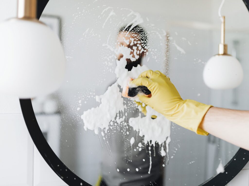 Gloved hand cleaning a soapy round mirror — things to clean with Dawn dish soap